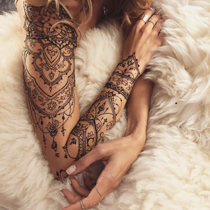 Γυναίκα με ωραίο χέρι-τατουάζ σε μαύρο χρώμα, πολλά μικρά στοιχεία, λουλουδένες προθέσεις, λευκή κουβέρτα, δαχτυλίδια