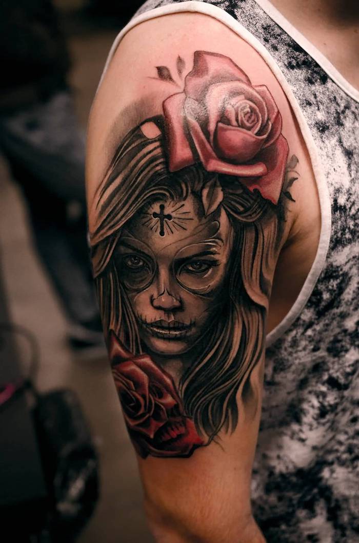 la catrina έννοια - ο άνθρωπος με ένα τατουάζ με δύο μεγάλα κόκκινα τριαντάφυλλα και μια νεαρή γυναίκα και ένα μικρό μαύρο σταυρό