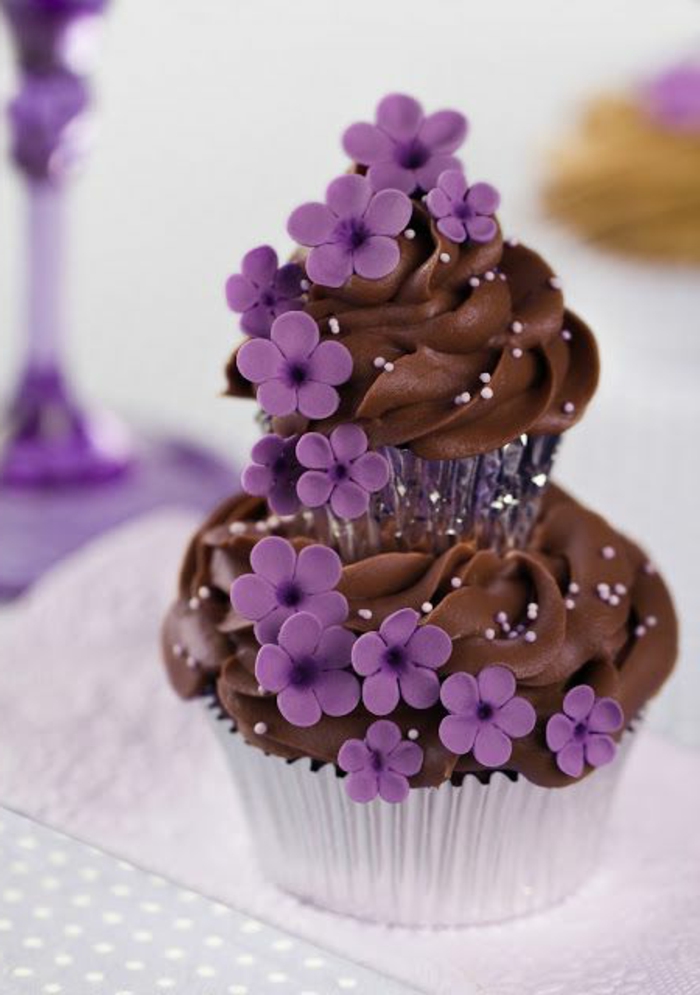 क्रीम और बैंगनी फूलों के साथ चॉकलेट कपकेक सजाने