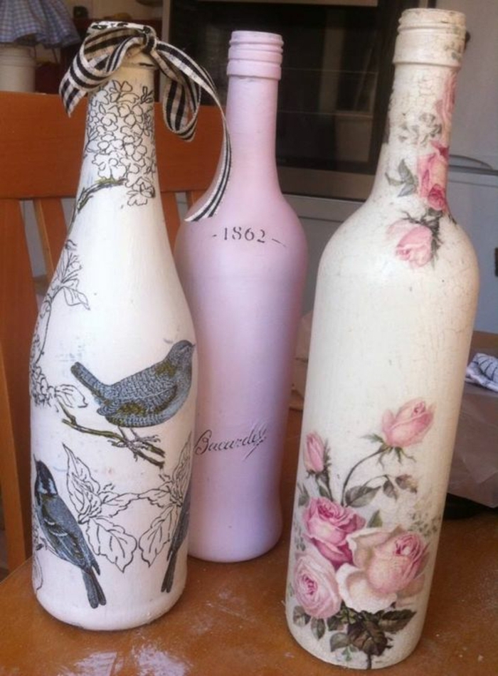 tres botellas con servilletas con flores rosadas y pájaros grises y un gorrión gris