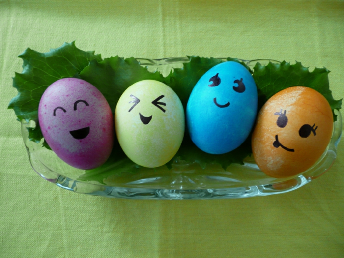 Oeufs de Pâques visages de quatre couleurs différentes dans une tasse avec des feuilles