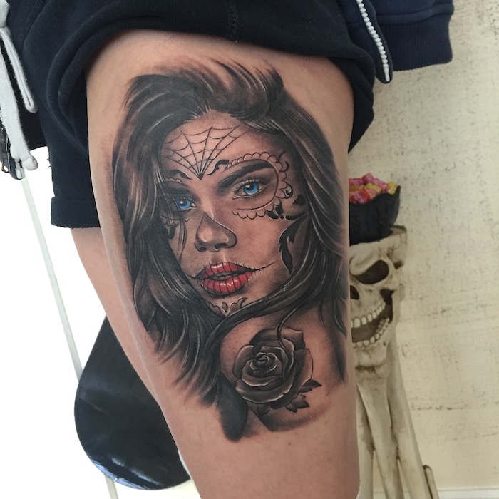 Πόδι με ένα τατουάζ La Catrina με μια νεαρή γυναίκα με κόκκινα χείλη και μπλε μάτια και μαύρο αράχνης