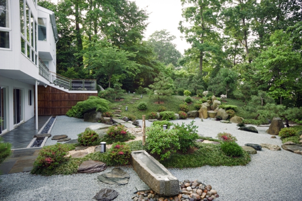 एक आधुनिक हवेली डिजाइन के लिए पत्थर और हरे पौधों के साथ विशाल बगीचा