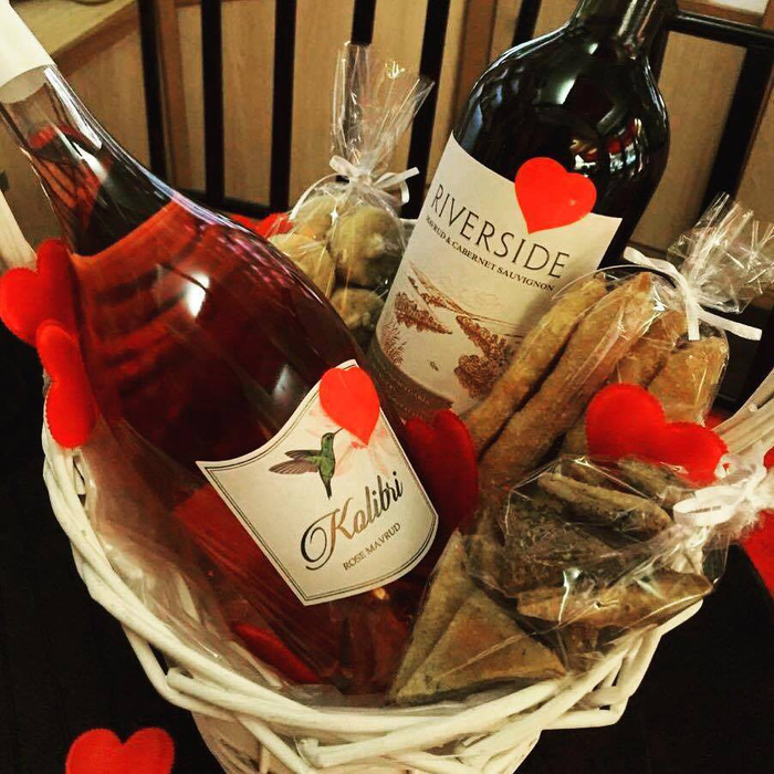 उपहार की टोकरी दो शराब की बोतलें, लाल शराब और गुलाब, मिठाई के साथ