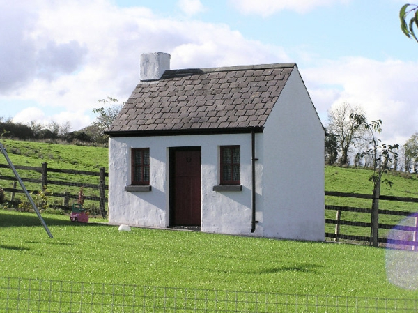 Pequeña casa construida de color gris - rodeada de hierba verde