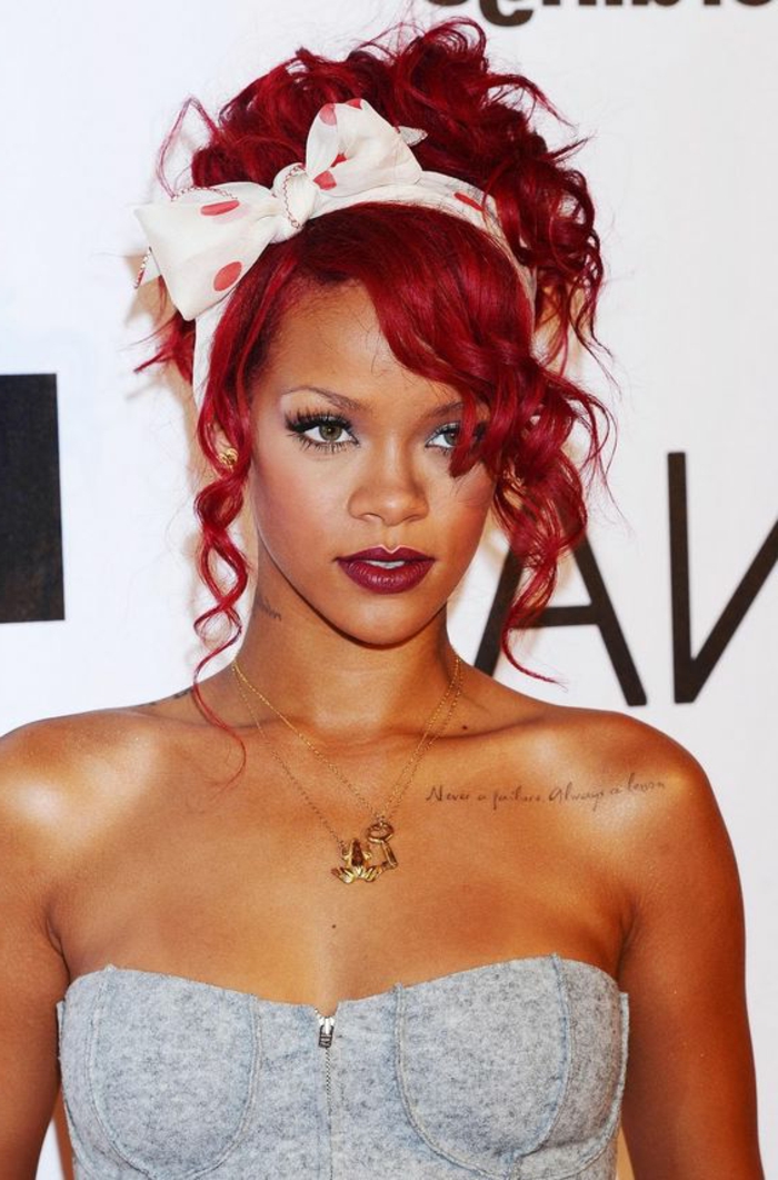 Rihanna con pelo rojo brillante, diadema blanca con puntos rojos, collares de oro, top gris