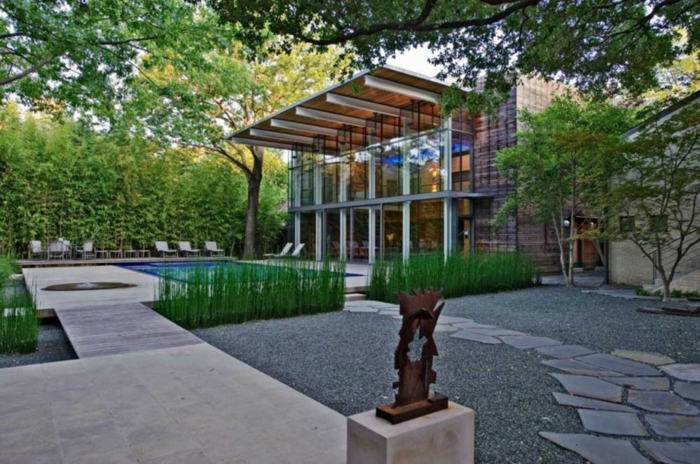 una casa con un moderno jardín frontal, fachada de vidrio, una piscina, escultura