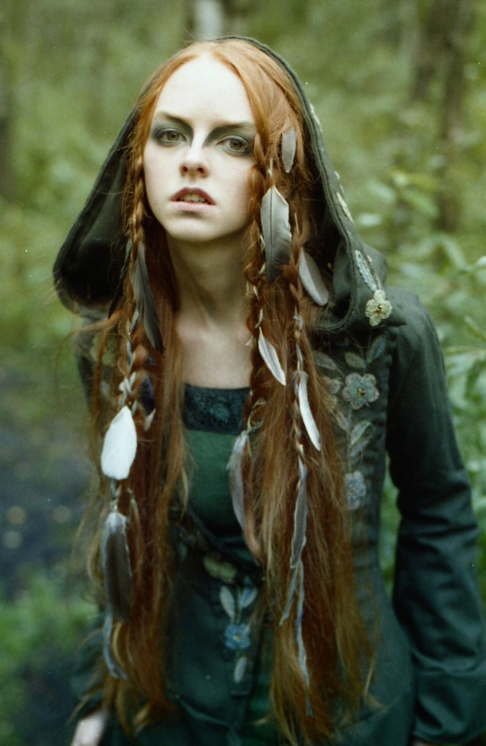 μια μάγισσα στο δάσος με φτερό στα μαλλιά κόκκινα μαλλιά, πράσινο φόρεμα - μεσαιωνικά χτενίσματα