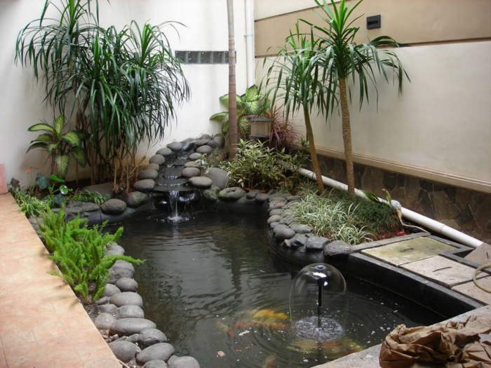 una hermosa fuente de agua con muchas piedras grises y palmeras exóticas - ejemplos de diseño de jardines
