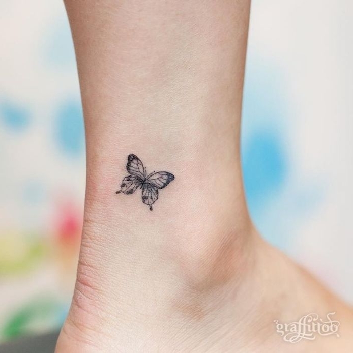 un lindo pequeño mini tatuaje negro minúsculo con una hermosa mariposa voladora negra en la pierna