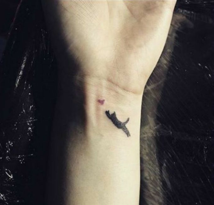 这是一只带有黑猫和小鸟的小纹身的手 - 用于在手腕上纹身的想法