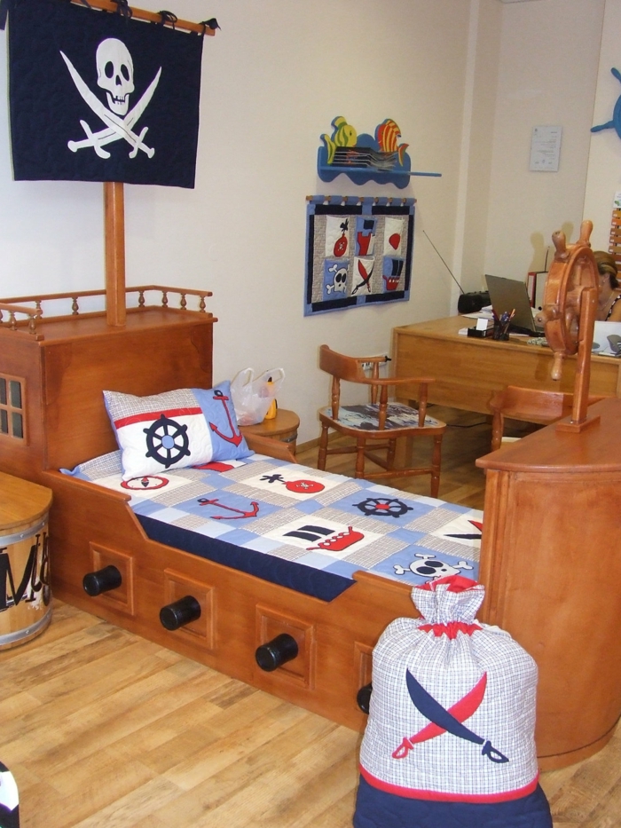 ένα κρεβάτι σαν πλοίο με σύμβολο κρανίου και μια τσάντα για τα παιχνίδια, γραφείο στο παρασκήνιο