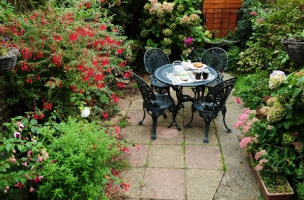 kaunis puutarha, jossa on monia värikkäitä kukkia ja pieni sohvapöytä, jossa on neljä tuolia