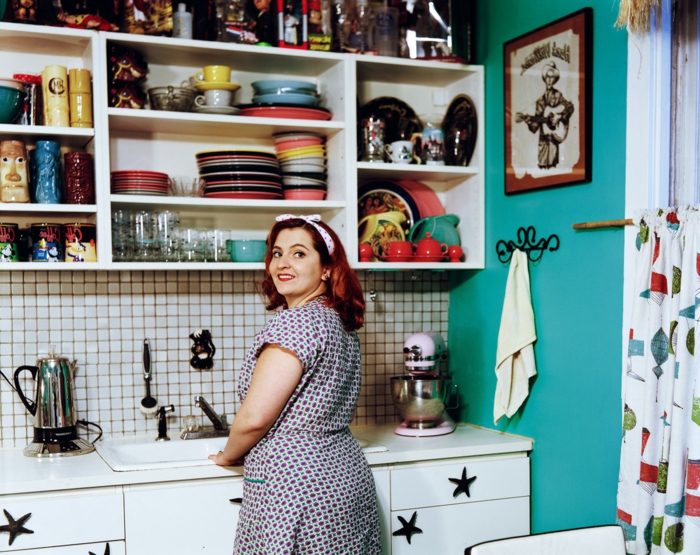 Decoración retro en la cocina: muchos platos, mural, paredes pintadas de azul, una mujer con un vestido de los años 50
