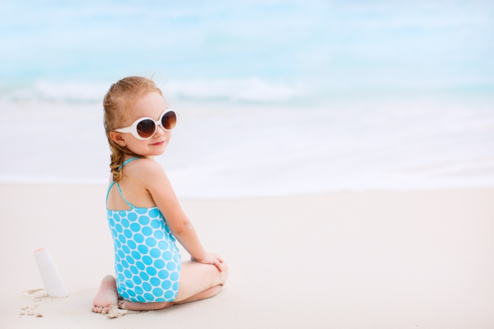 उष्णकटिबंधीय समुद्र तट पर सूरज क्रीम की बोतल वाली छोटी लड़की