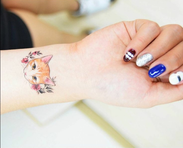 一只手，手指，彩色指甲油，手腕上的猫纹身，一只小猫，红色的花朵