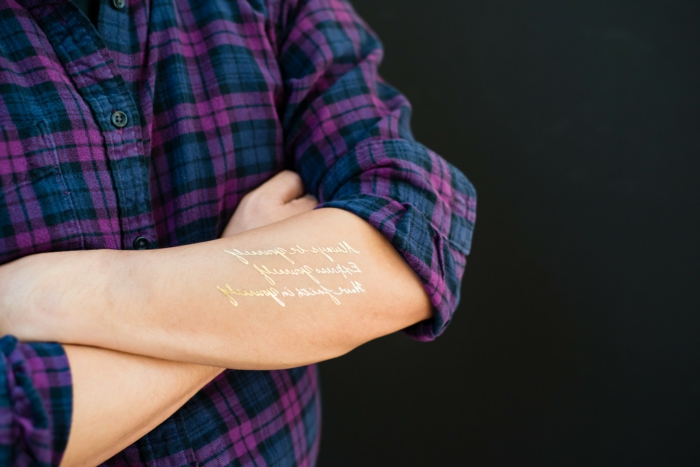 kauniita tatuointeja kultaisia ​​sanoja seisoo käsivarteen ja kaunistaa kehon violetti sininen paita