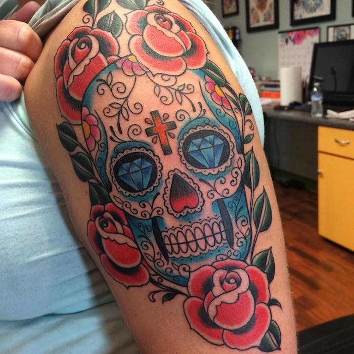 Mexikói koponya tetoválás kék gyémántokkal és fehér fogakkal, narancssárga kereszt és ibolya virágokkal - koponya rózsákkal tetoválással