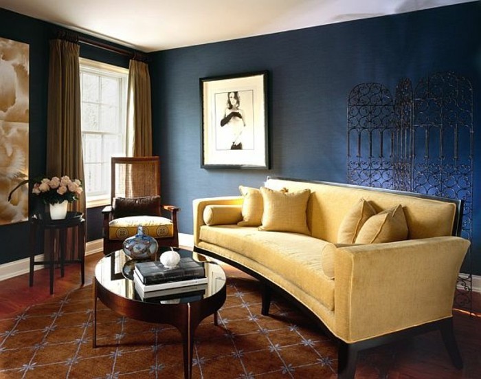 Falfesték-kék színben falak színes falakon halványsárga dívány-párna mintás szőnyeg fából készült padlóburkolat, fából készült szék, ovális asztal üveg dekoratív váza